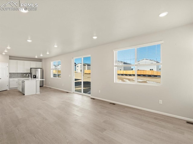 unfurnished living room with light wood-type flooring, a healthy amount of sunlight, and sink