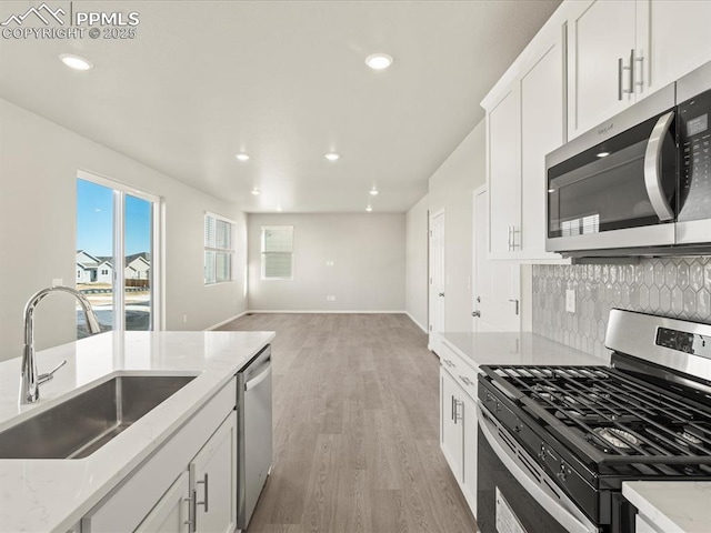 kitchen featuring stainless steel appliances, light wood-type flooring, light stone countertops, white cabinets, and sink