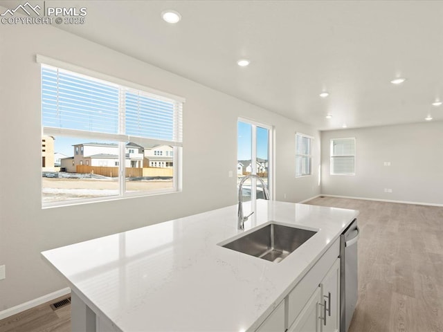 kitchen featuring light hardwood / wood-style floors, an island with sink, stainless steel dishwasher, white cabinets, and sink