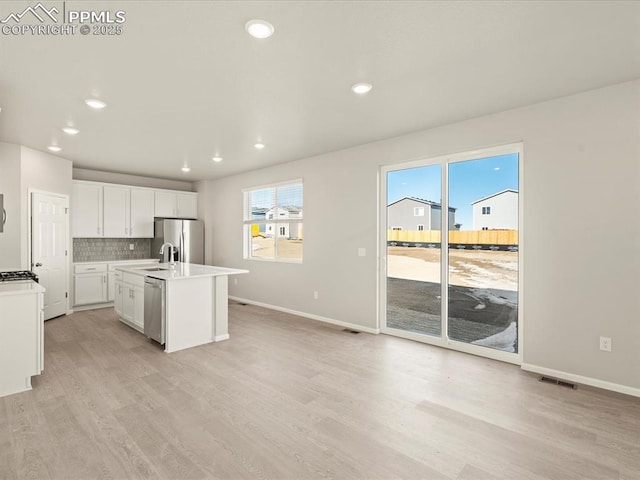 kitchen with stainless steel appliances, tasteful backsplash, a kitchen island with sink, white cabinets, and light hardwood / wood-style flooring