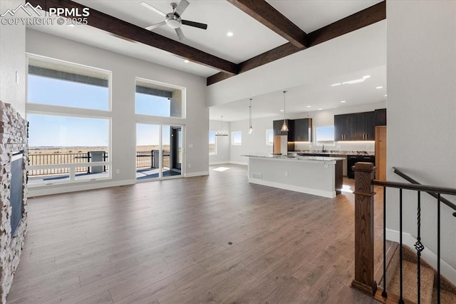 living room featuring a towering ceiling, beamed ceiling, sink, ceiling fan, and dark wood-type flooring