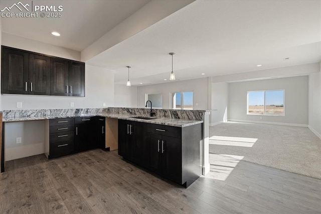 kitchen featuring pendant lighting, sink, light stone counters, kitchen peninsula, and light wood-type flooring