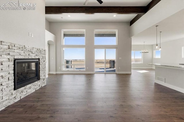 unfurnished living room featuring dark wood-type flooring, a fireplace, beamed ceiling, and ceiling fan with notable chandelier