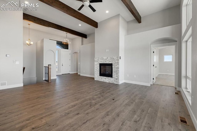 unfurnished living room featuring beam ceiling, a towering ceiling, dark hardwood / wood-style floors, a fireplace, and ceiling fan with notable chandelier