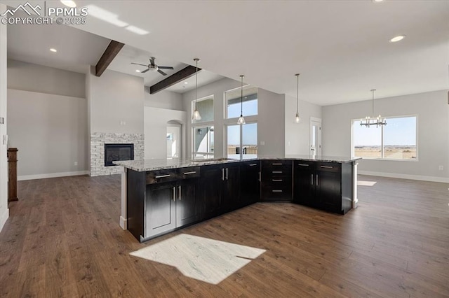 kitchen with pendant lighting, a fireplace, light stone countertops, and a kitchen island with sink