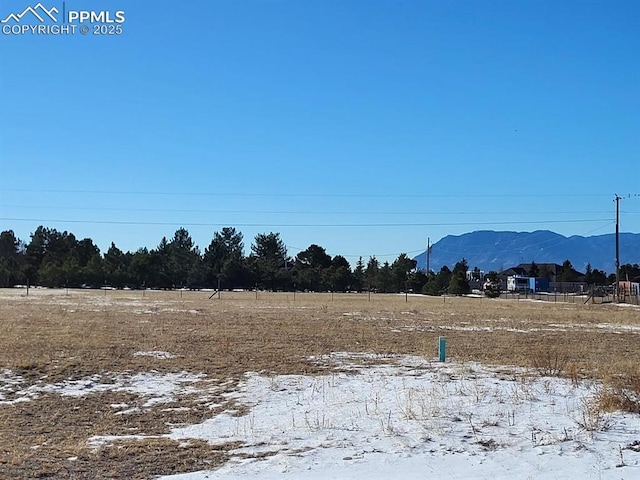 snowy yard with a rural view and a mountain view