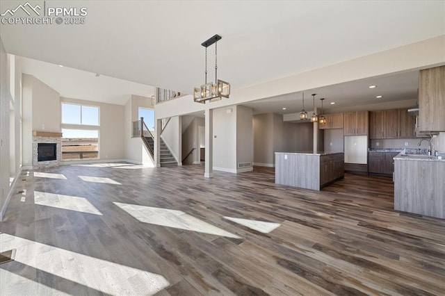 unfurnished living room with an inviting chandelier, a fireplace, dark wood-type flooring, and sink