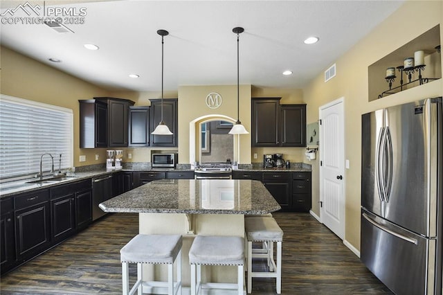 kitchen featuring appliances with stainless steel finishes, a kitchen island, decorative light fixtures, dark wood-type flooring, and sink