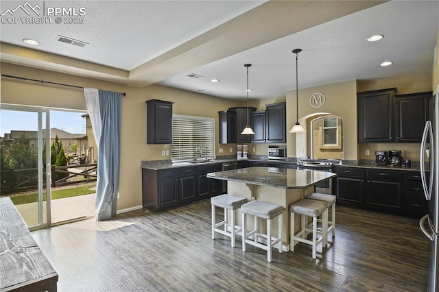 kitchen with stainless steel appliances, dark wood-type flooring, dark stone counters, hanging light fixtures, and a center island