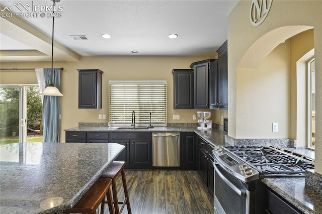 kitchen with hanging light fixtures, dark stone counters, sink, and stainless steel appliances