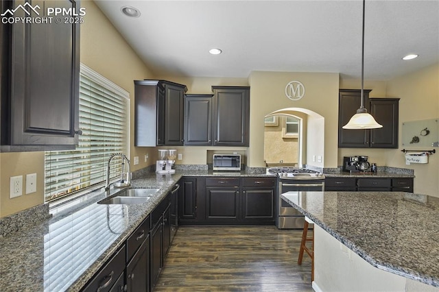 kitchen with gas stove, decorative light fixtures, dark hardwood / wood-style flooring, sink, and a breakfast bar area