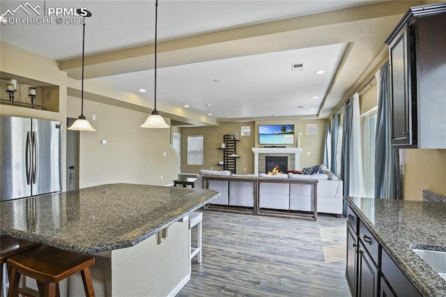 kitchen with a fireplace, a kitchen bar, hanging light fixtures, dark wood-type flooring, and stainless steel fridge