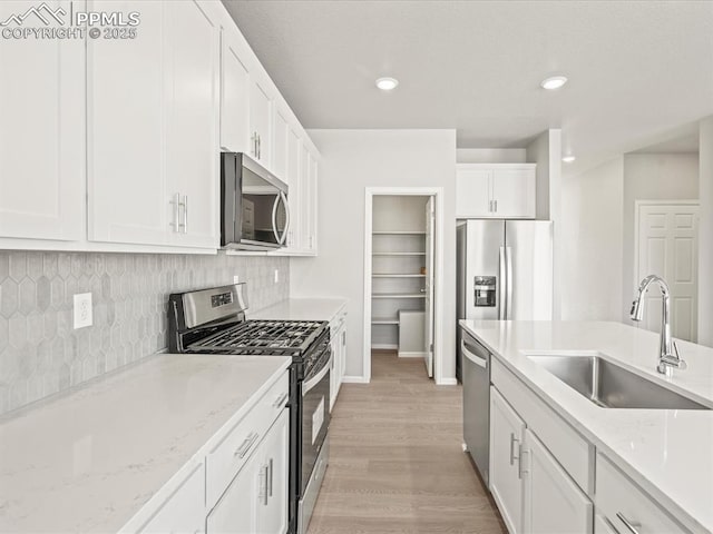 kitchen featuring light stone countertops, white cabinets, stainless steel appliances, sink, and light hardwood / wood-style flooring