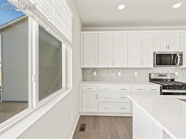 kitchen featuring decorative backsplash, white cabinetry, light hardwood / wood-style flooring, light stone countertops, and appliances with stainless steel finishes