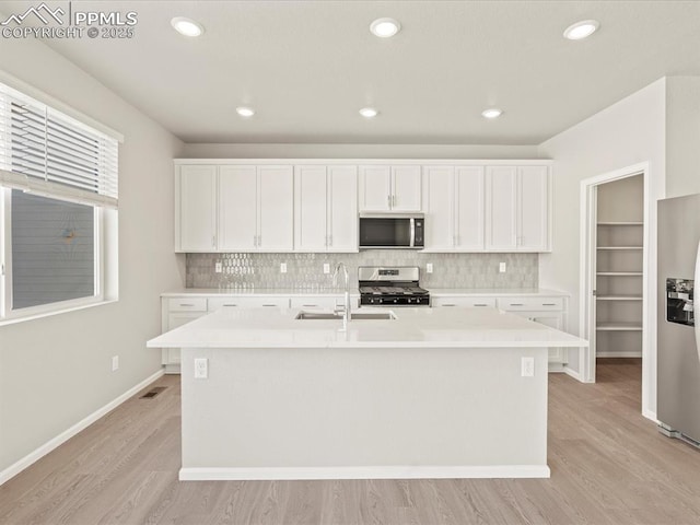 kitchen with an island with sink, sink, stainless steel appliances, and white cabinetry