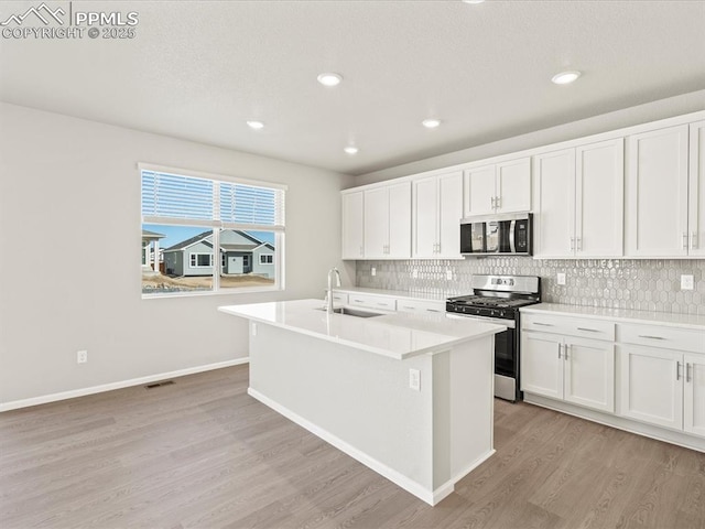 kitchen with sink, white cabinetry, light hardwood / wood-style flooring, a kitchen island with sink, and appliances with stainless steel finishes