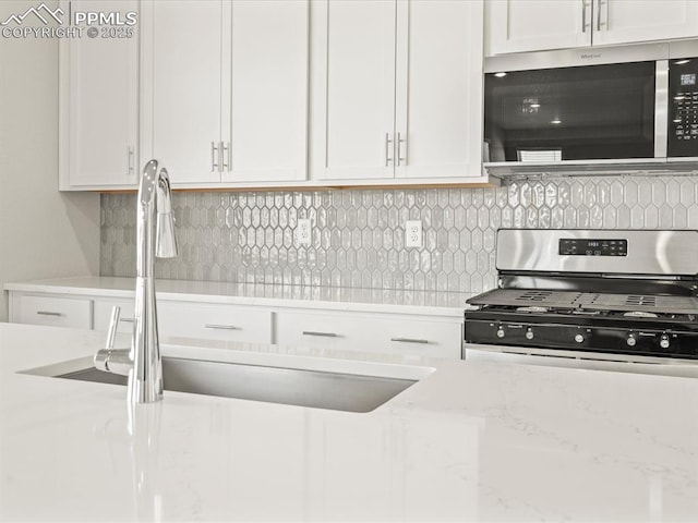 kitchen with light stone counters, sink, white cabinetry, and appliances with stainless steel finishes