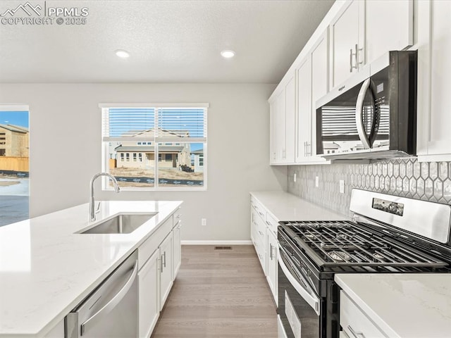 kitchen with backsplash, sink, appliances with stainless steel finishes, white cabinets, and light stone counters