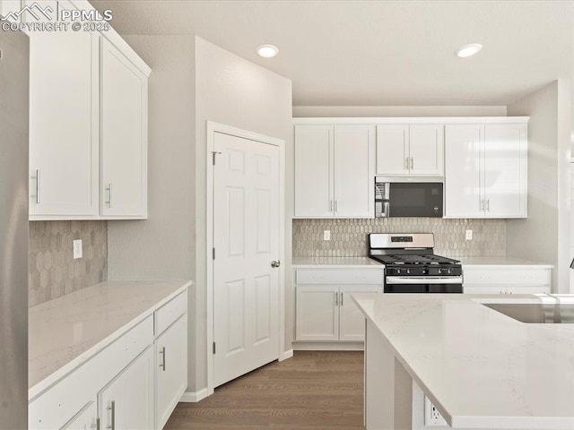 kitchen featuring light hardwood / wood-style floors, stainless steel appliances, decorative backsplash, light stone countertops, and white cabinets