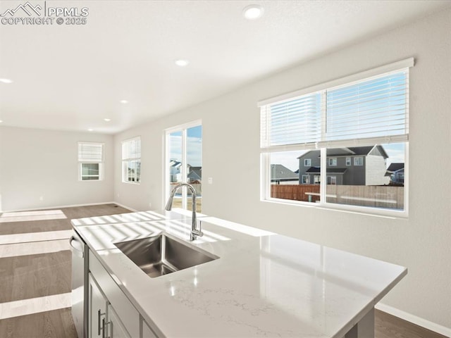 kitchen featuring a kitchen island, sink, dark hardwood / wood-style floors, light stone counters, and stainless steel dishwasher