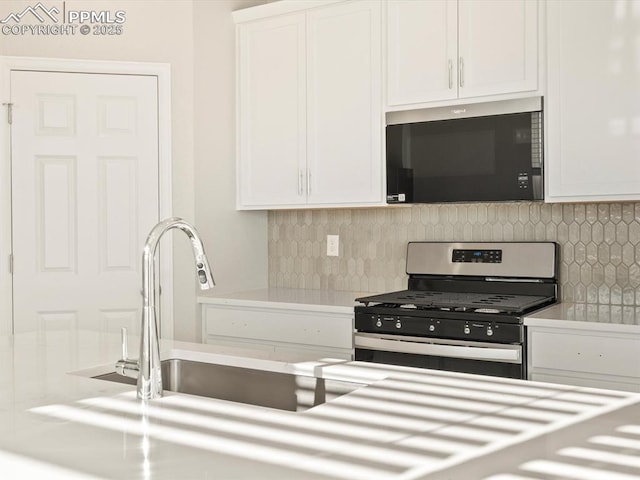 kitchen featuring stainless steel gas range, backsplash, white cabinets, and sink