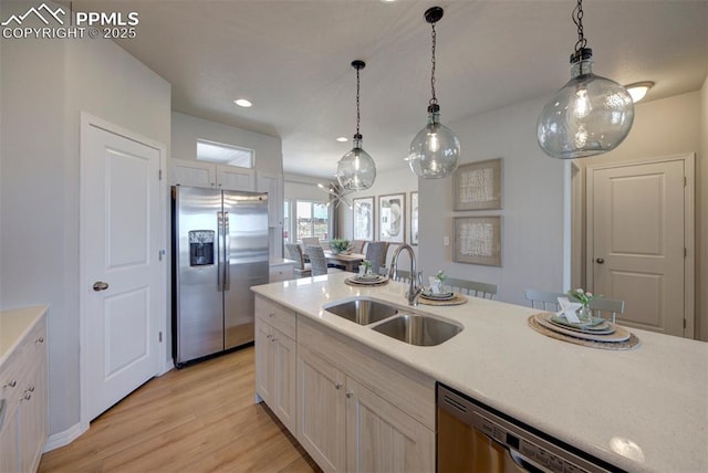 kitchen with appliances with stainless steel finishes, light hardwood / wood-style floors, pendant lighting, and sink