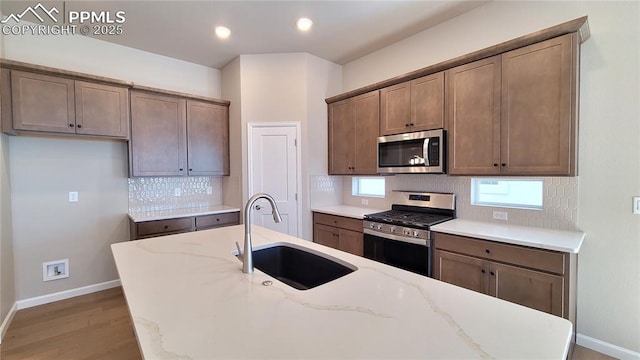 kitchen featuring light wood-type flooring, light stone counters, stainless steel appliances, sink, and a center island with sink