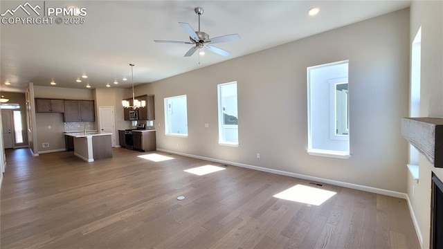 unfurnished living room featuring wood-type flooring, ceiling fan with notable chandelier, and sink