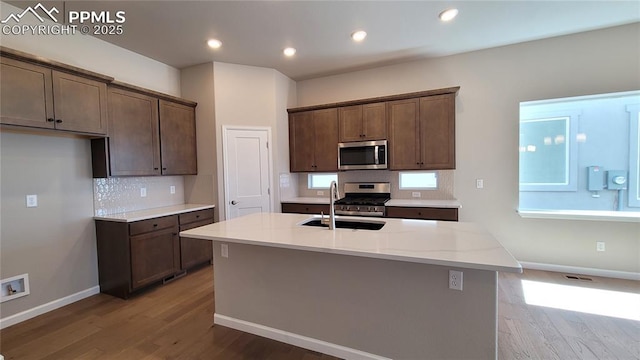 kitchen with sink, hardwood / wood-style flooring, an island with sink, light stone counters, and stainless steel appliances