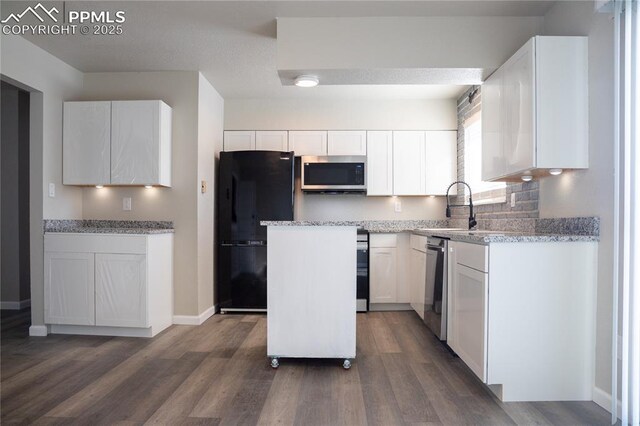 kitchen with stainless steel appliances, sink, white cabinetry, light stone countertops, and a kitchen island