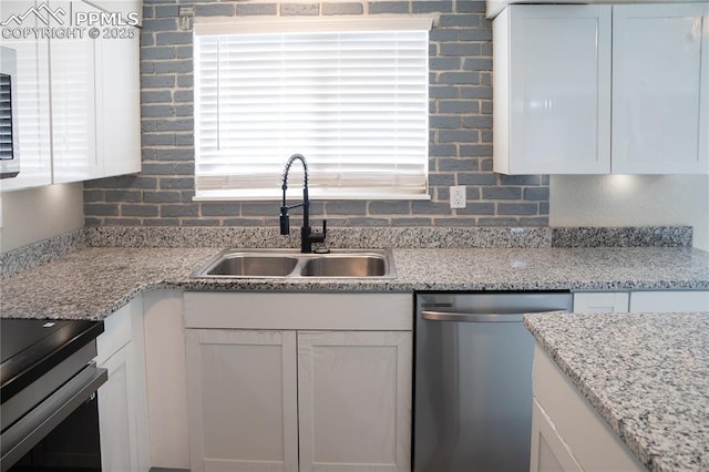 kitchen featuring light stone counters, stainless steel dishwasher, white cabinetry, and sink