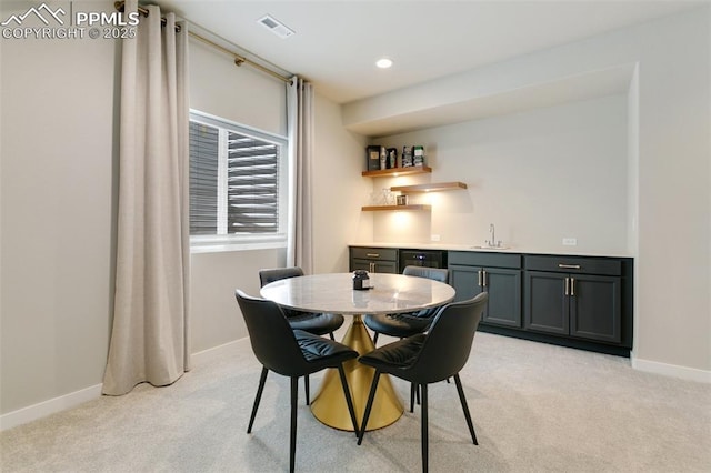 dining room featuring wet bar, light carpet, visible vents, and baseboards