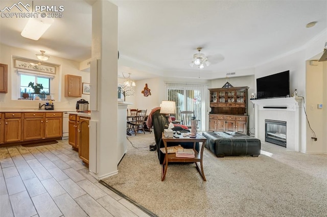 carpeted living room with ceiling fan with notable chandelier, a tile fireplace, and sink