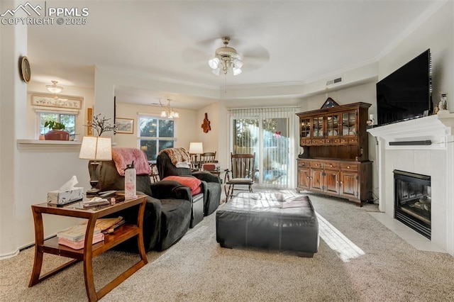 carpeted living room featuring ceiling fan with notable chandelier, a tile fireplace, and a tray ceiling