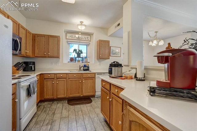 kitchen with white appliances, hanging light fixtures, light hardwood / wood-style floors, an inviting chandelier, and sink