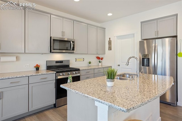 kitchen featuring light stone counters, sink, stainless steel appliances, and an island with sink