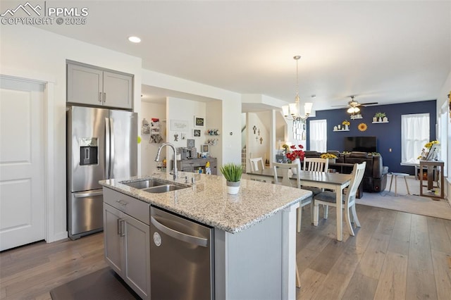 kitchen with a center island with sink, sink, appliances with stainless steel finishes, gray cabinetry, and ceiling fan with notable chandelier