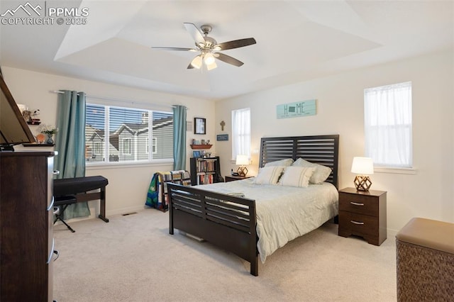 bedroom with ceiling fan, light colored carpet, a raised ceiling, and multiple windows