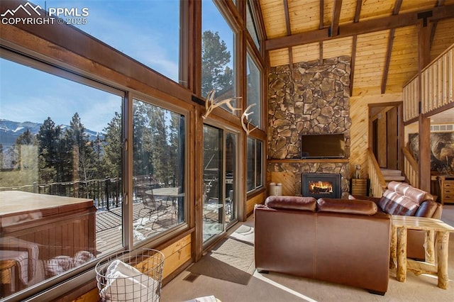 sunroom featuring a mountain view, a healthy amount of sunlight, wood ceiling, and a stone fireplace