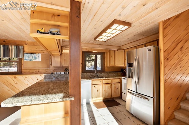 kitchen with light brown cabinets, white appliances, wooden walls, and light tile patterned floors