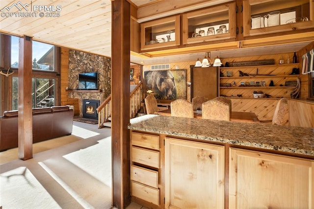 bar featuring light carpet, light stone countertops, wooden walls, a fireplace, and an inviting chandelier