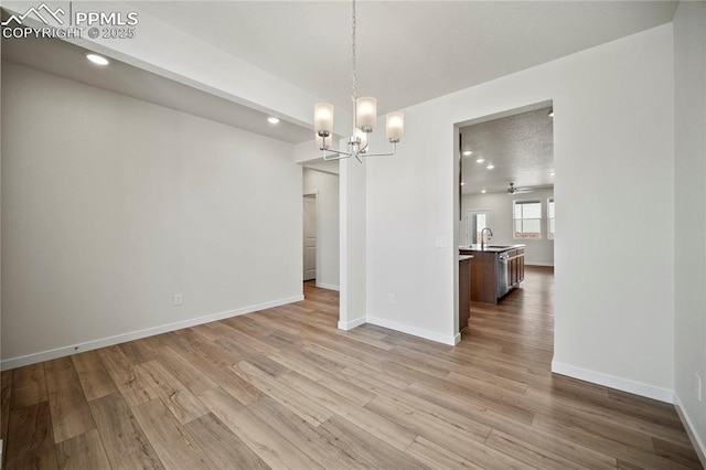 unfurnished dining area featuring ceiling fan with notable chandelier, light hardwood / wood-style floors, and sink