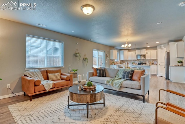 living room with light hardwood / wood-style floors, a textured ceiling, and a notable chandelier