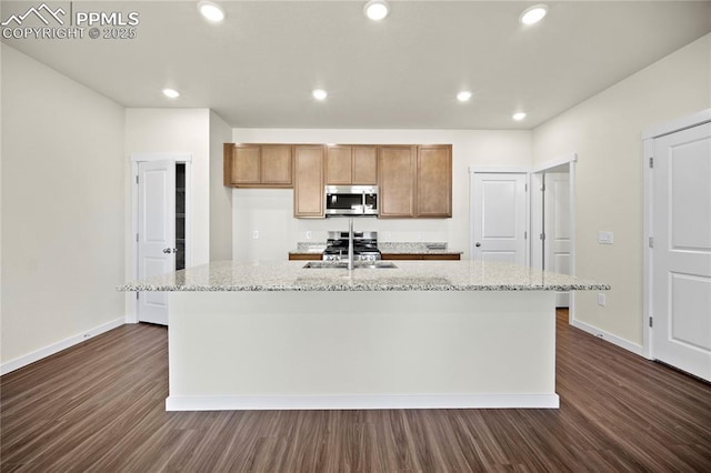 kitchen featuring dark hardwood / wood-style flooring, light stone counters, a kitchen island with sink, and appliances with stainless steel finishes