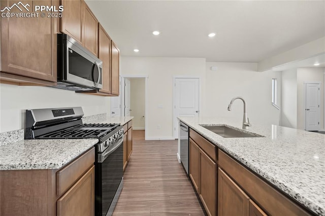 kitchen with a kitchen island with sink, sink, light stone countertops, appliances with stainless steel finishes, and light hardwood / wood-style floors