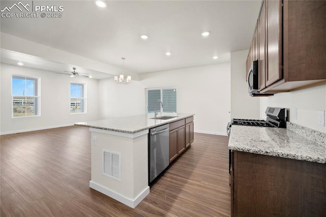 kitchen with a center island with sink, sink, decorative light fixtures, light stone counters, and stainless steel appliances