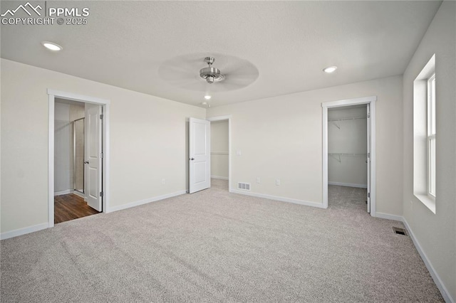 unfurnished bedroom featuring carpet floors, a closet, a spacious closet, and ceiling fan