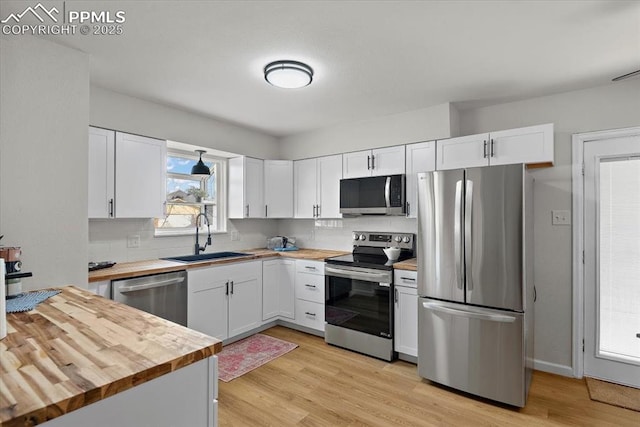 kitchen featuring white cabinets, appliances with stainless steel finishes, butcher block counters, and sink