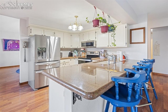 kitchen featuring sink, light hardwood / wood-style flooring, kitchen peninsula, a chandelier, and appliances with stainless steel finishes