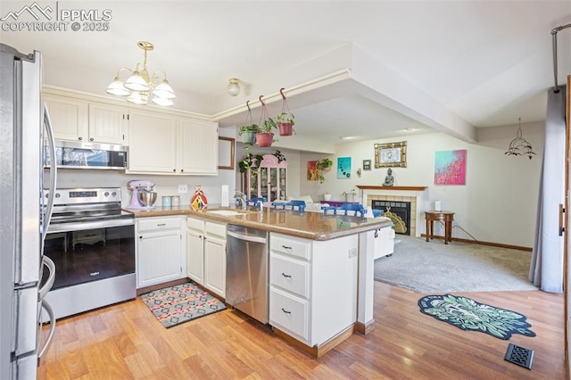 kitchen featuring white cabinets, hanging light fixtures, kitchen peninsula, stainless steel appliances, and a tiled fireplace